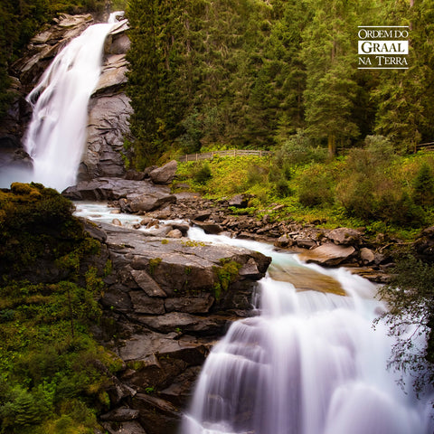 Foto de cachoeira com duas cortinas de água, dois degraus de queda em meio a margens de pedra e contorno natureza verdejante.