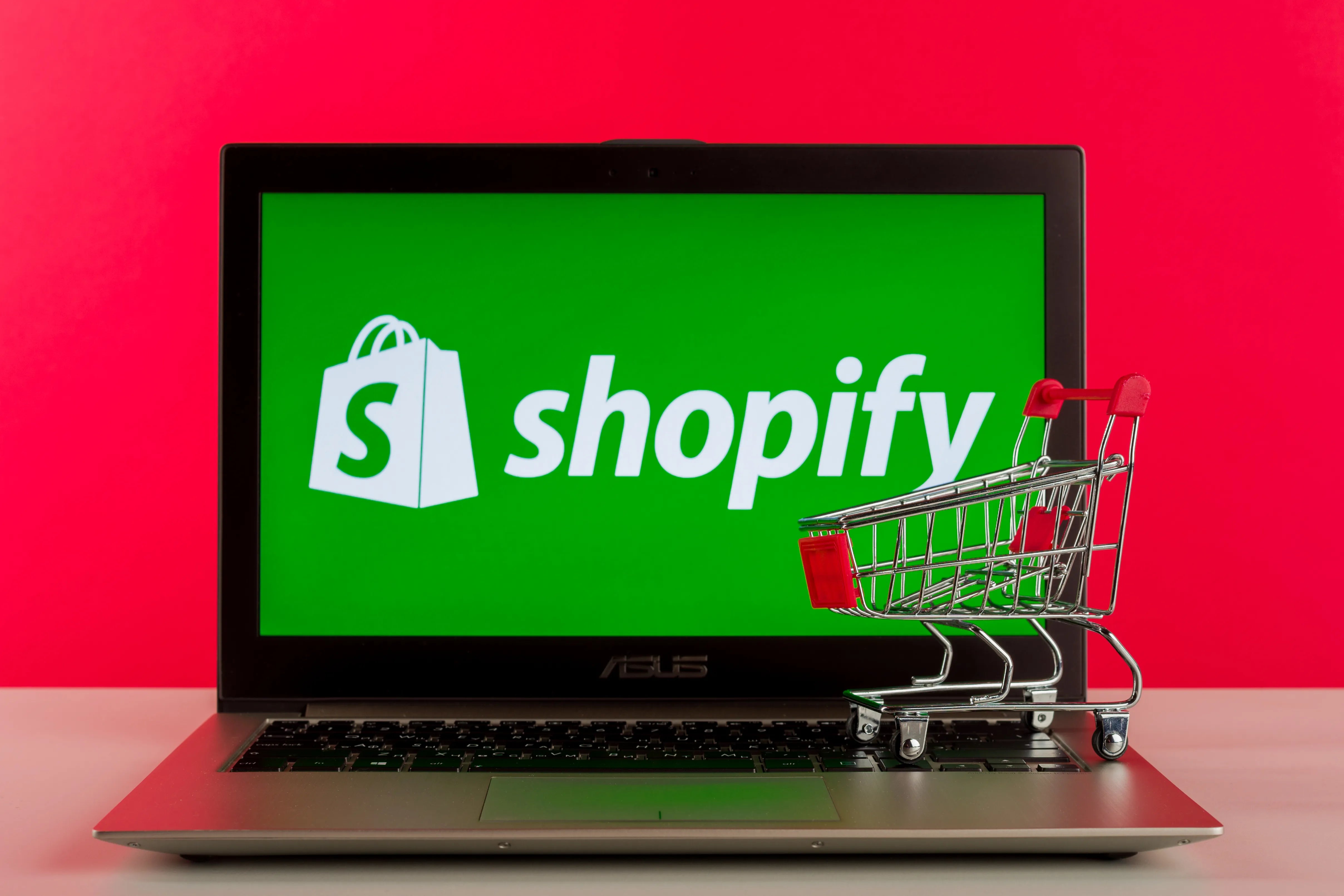 A photo that showcases the Shopify logo on a laptop screen, with a miniature shopping cart nearby.