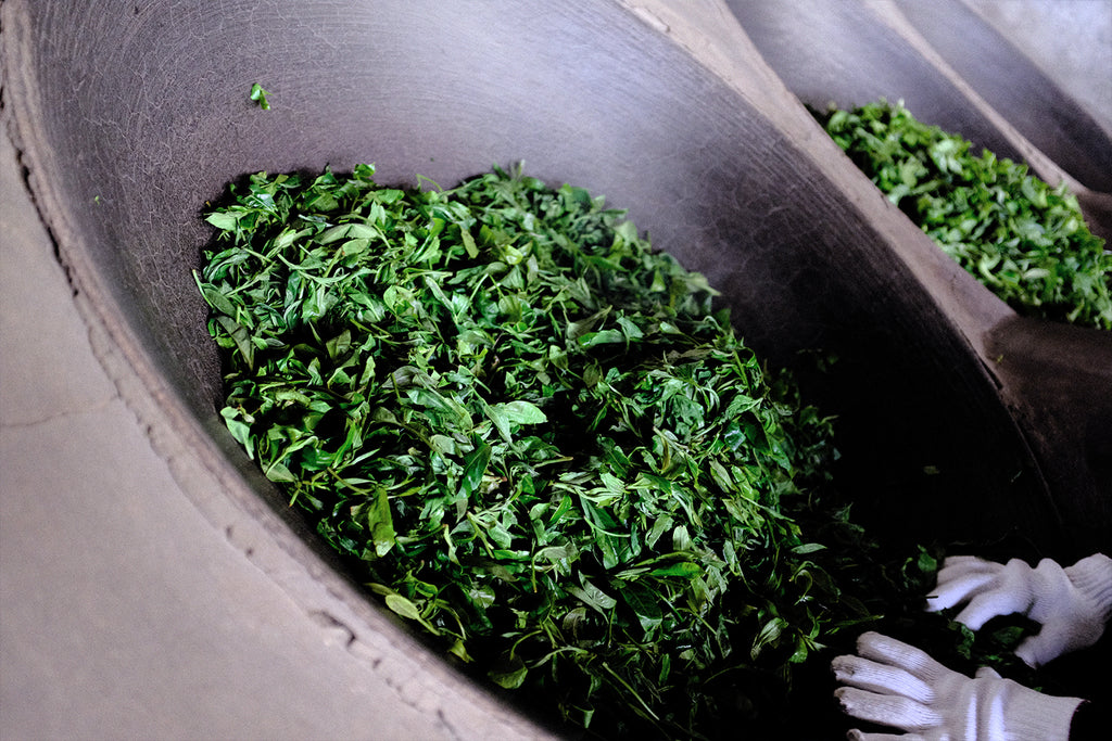 Raw puerh tea leaves being fried in a wok by hand