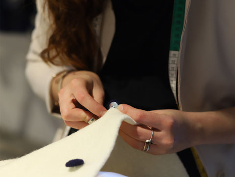 Inside the Marta Scarampi atelier, the seamstress completes a cape with a button