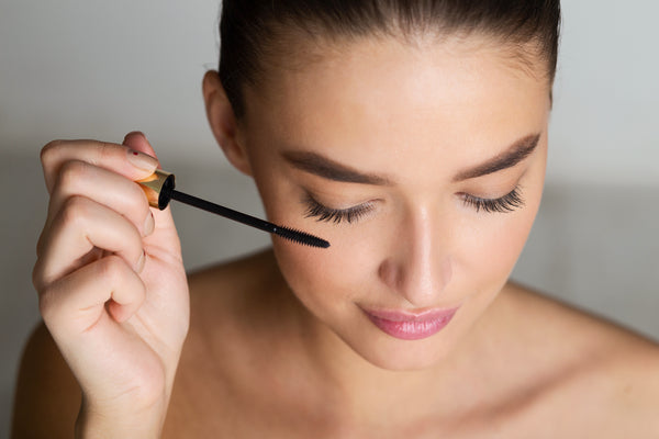 Woman with long eyelashes putting on mascara. Cartel Lash