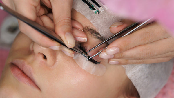 Woman getting lash extensions from lash tech. Cartel Lash