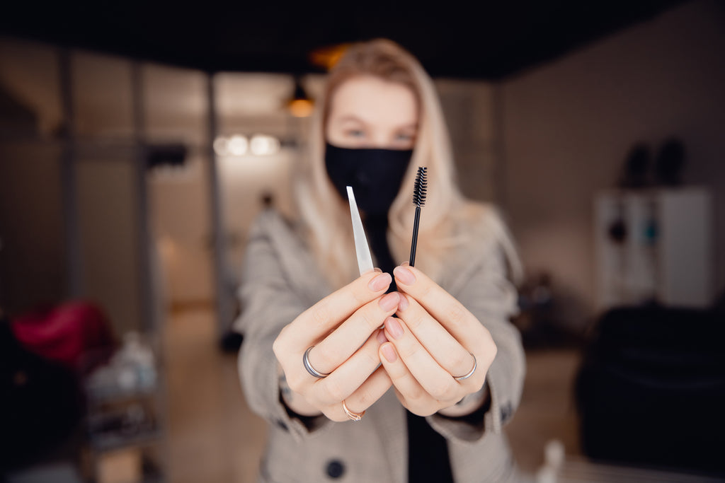 Woman holding lash extension supplies such as tweezers and mascara wand. Cartel Lash