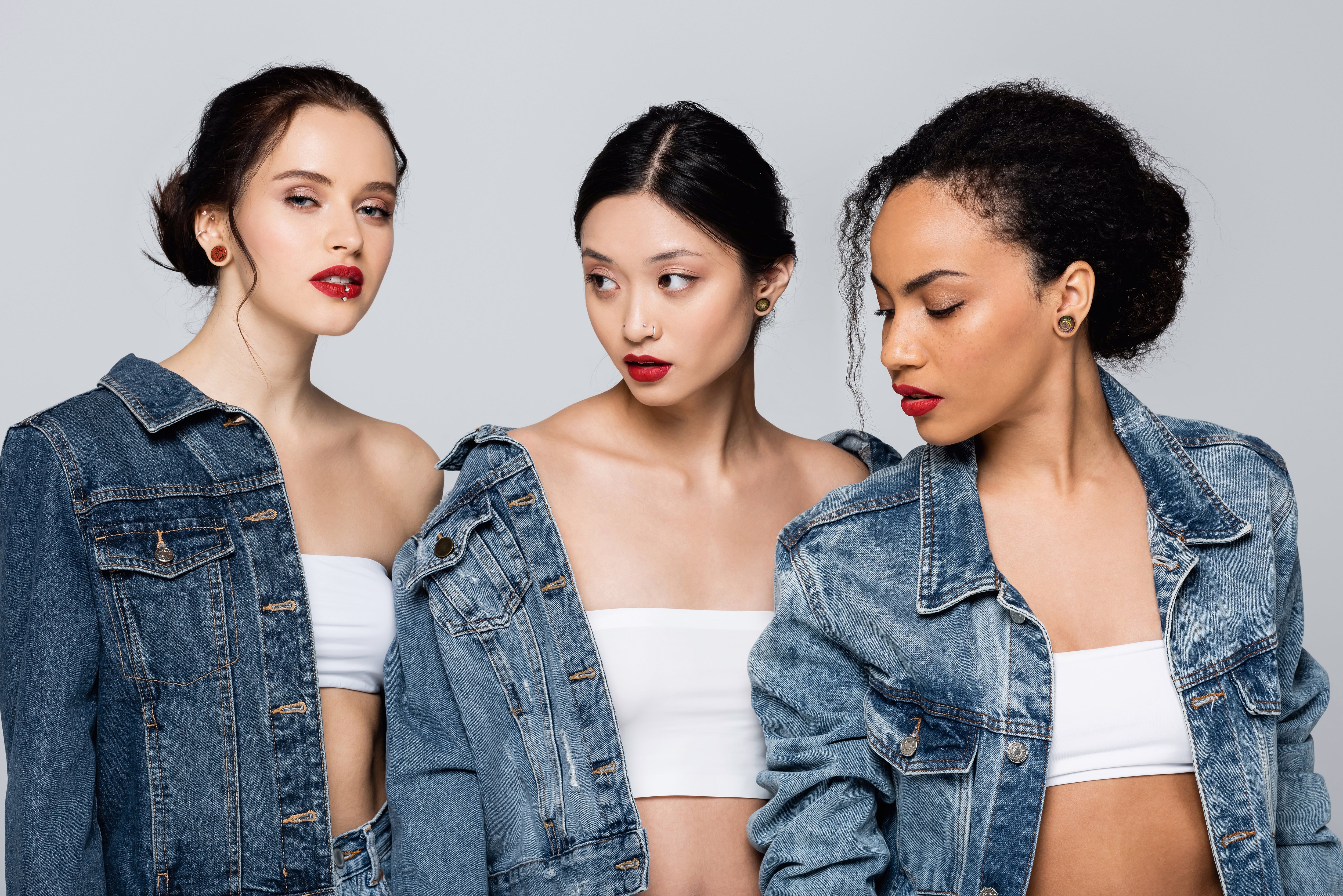 Three young women wear matching denim jackets and body piercing jewelry from bm25 for womens history month
