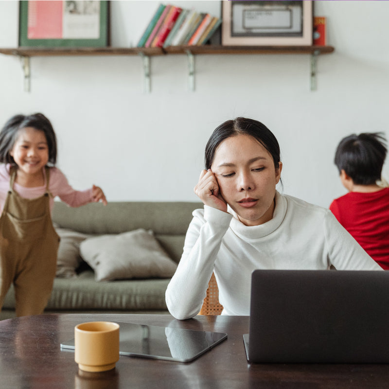 woman looking at laptop with children behind her