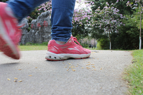 Woman with pink shoes walking through a park.