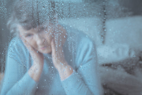 Looking through window at woman with hands on her face.