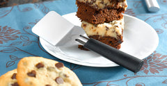 A RADA Mini Server spatula with a black resin handle next to a couple fudge bars on a white plate next to some cookies