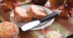 A RADA Cutlery Party Spreader next to two slices of bread on a white plate near a muffin and serving of butter