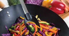A RADA Non-Scratch Spoon lifting a couple slices of peppers from a wok bowl