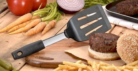 A Rada Non-Scratch Spatula propped up next to a hamburger with a sesame seed bun, french fries, carrots and red tomatoes