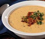 A hearty bowl of cheesy soup topped with chopped parsley and bacon