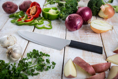 A RADA stainless steel French Chef Knife with a black resin handle in the middle of some sliced potatoes, cilantro, garlic, red peppers and red onions