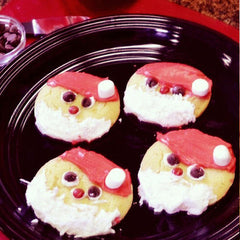 Santa Christmas sugar cookies with red stocking hats and white beards laid out on a black platter