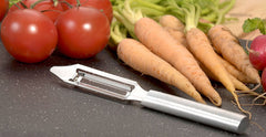 A RADA stainless steel Vegetable Peeler with a silver brushed aluminum handle next to some carrots and a couple red tomatoes