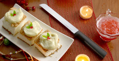 A RADA Cutlery six inch bread knife with a black handle next to three dessert bars with white frosting on a white platter next to some orange slices