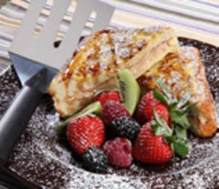 Several slices of crisp french toast sprinkled with sugar and surrounded by strawberries and blackberries next to a RADA Turnover stainless steel spatula