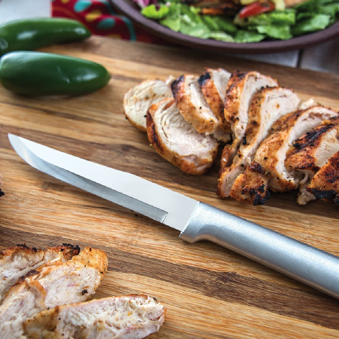 Rada Cutlery silver handle Stubby Butcher on a cutting board with sliced pork and peppers.