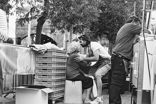 Man holding older woman on a chair in a market.