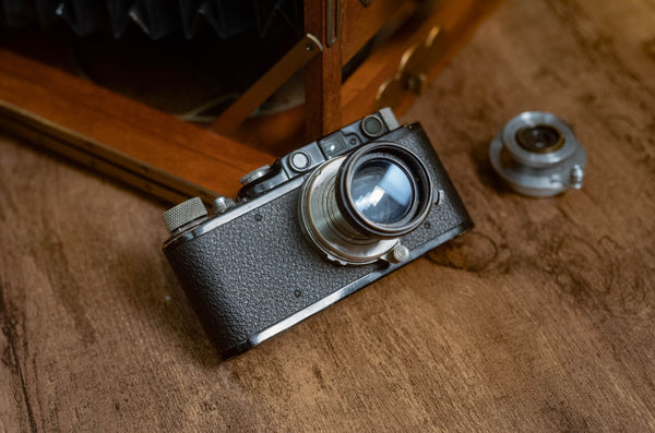 An early Leica rangefinder camera laying on a wooden table.