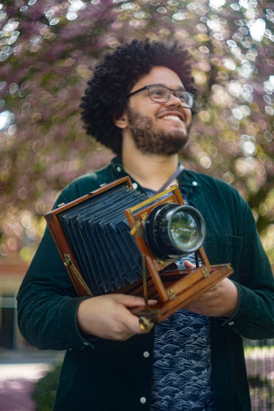 A man with an afro holding The Adam's and Co. Half Plate camera with the 8" f/2.9 Dallmeyer Pentac.