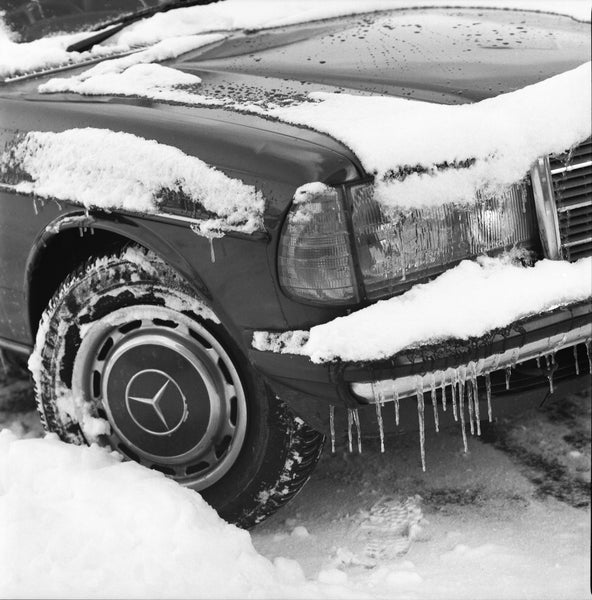 The corner of a car in the snow, in black and white.
