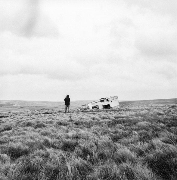 A man standing next to a broken down plane in a field in black-and-white.