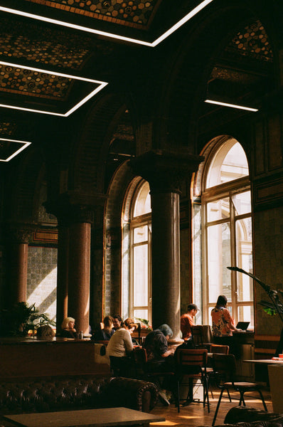 A series of large windows, with light shining on the patrons of a cafe.