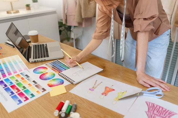 A fashion designer's workplace featuring design drafts, a color palette, and various designs spread across the desk.