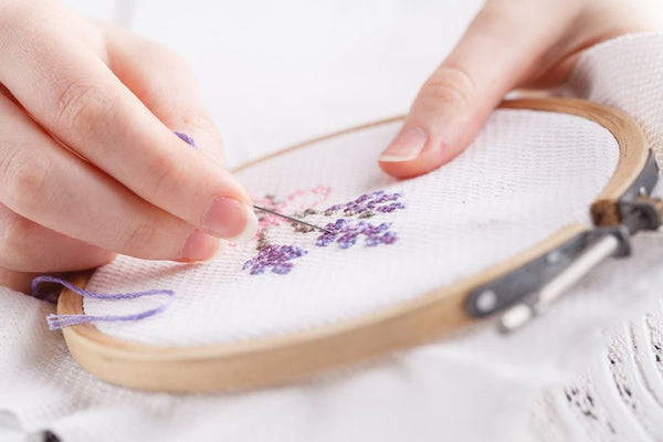 A woman's hand engaged in the art of hand-stitching an embroidery design, showcasing a DIY crafting process.