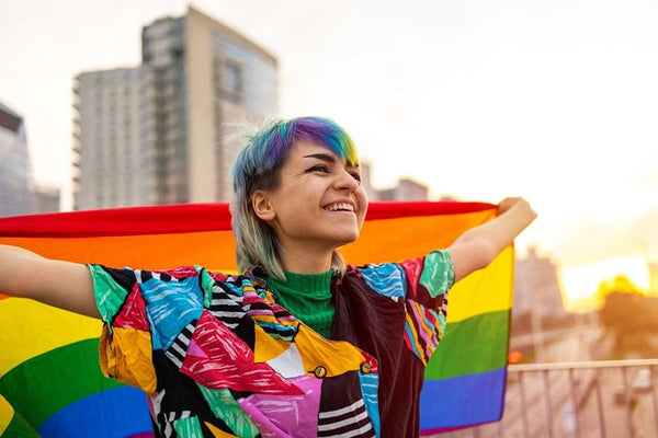 A non-binary individual waving a colorful pride flag with happiness, symbolizing gender expression and pride.