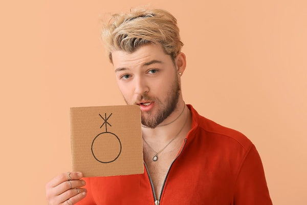 A non-binary individual with a mustache holding a gender symbol sign, advocating for gender pronouns education.