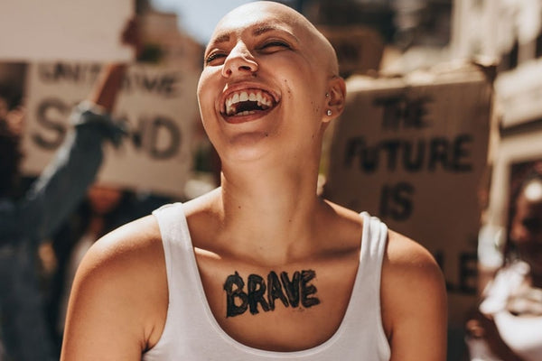 Un individuo alegre y no binario con la cabeza calva, que participa activamente en una protesta feminista, enfatizando la igualdad de género y la importancia de la educación feminista.