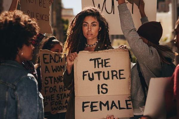 Un grupo de mujeres con un cartel que dice "El futuro es femenino" en una protesta feminista, que simboliza la promoción y la educación de los derechos de las mujeres.