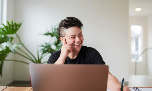 Transgender manager in a professional working environment, exuding happiness and confidence. Seated with a laptop and notebook, ready for a meeting, his face reflects a blend of focus and satisfaction, symbolizing leadership and positivity in the workplace.