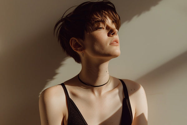 Non-binary androgynous individual with a masculine tomboy style, captured in a full body view. They exhibit a clean haircut and utilize chest binding to achieve a flattened chest appearance. Dressed in a black sports bra, their stance and expression radiate confidence, embodying a strong sense of self-assurance and identity.