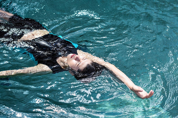 A non-binary androgynous tomboy with a clean haircut, wearing a black swimming chest binder, swimming gracefully in a pool from an underwater perspective.