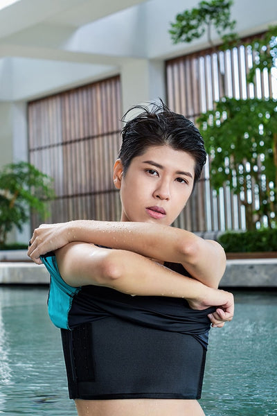 A non-binary androgynous tomboy with a clean haircut, wearing a black swimming chest binder, swimming gracefully in a pool from an underwater perspective.