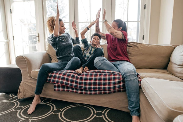 A joyful lesbian family, celebrating their transgender child's transition journey while sitting on a living room sofa.