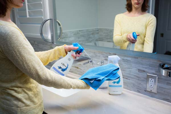 woman is spraying AspenClean natural bathroom cleaner on the bathroom microfiber cloth