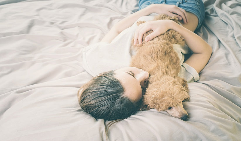 A woman is cuddling up with her pet on the bed 