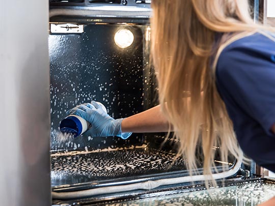 A lady is using Natural SuperScrub Scouring Powder to clean the oven