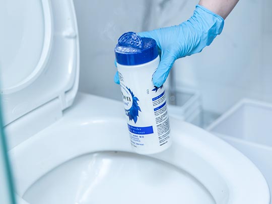 A person is using the Natural SuperScrub Scouring Powder to clean the toilet