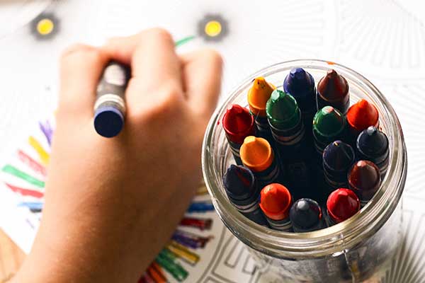 Kid is drawing with colorful crayons 