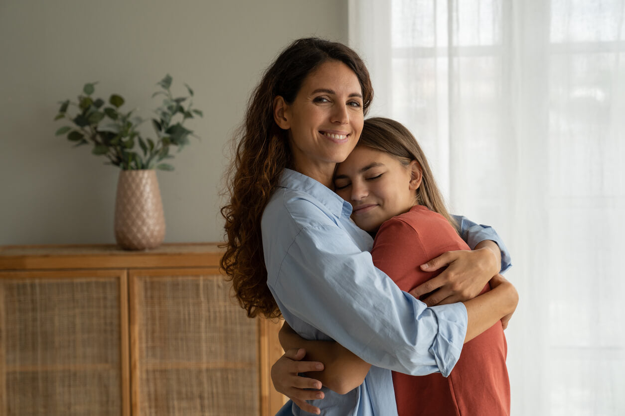 Mum and teen girl hugging at home.