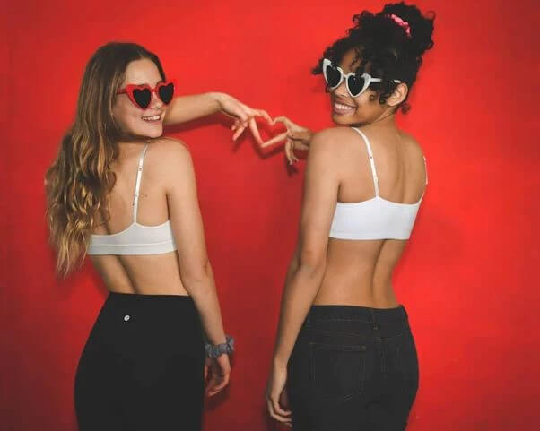 Two teenage girls wearing white bralettes from Bleuet making a heart sign with their hands.
