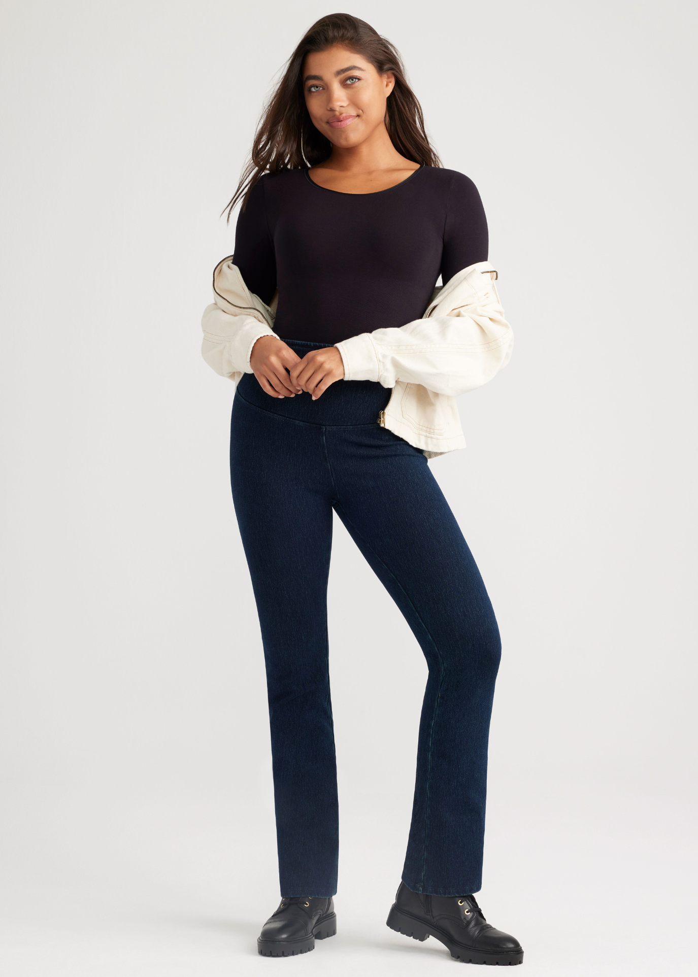 long sleeve shaping thong bodysuit - outlast® seamless in Black , denim bootcut shaping legging in True Indigo and a zip up in Ivory worn by a woman standing facing forward with arms at waist Yummie