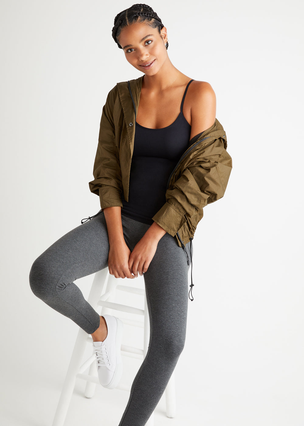 non-shaping camisole - seamless in Black, rachel shaping legging - cotton stretch in heather Grey and  a green jacket worn by a woman sitting on a stool with her arms in front Yummie