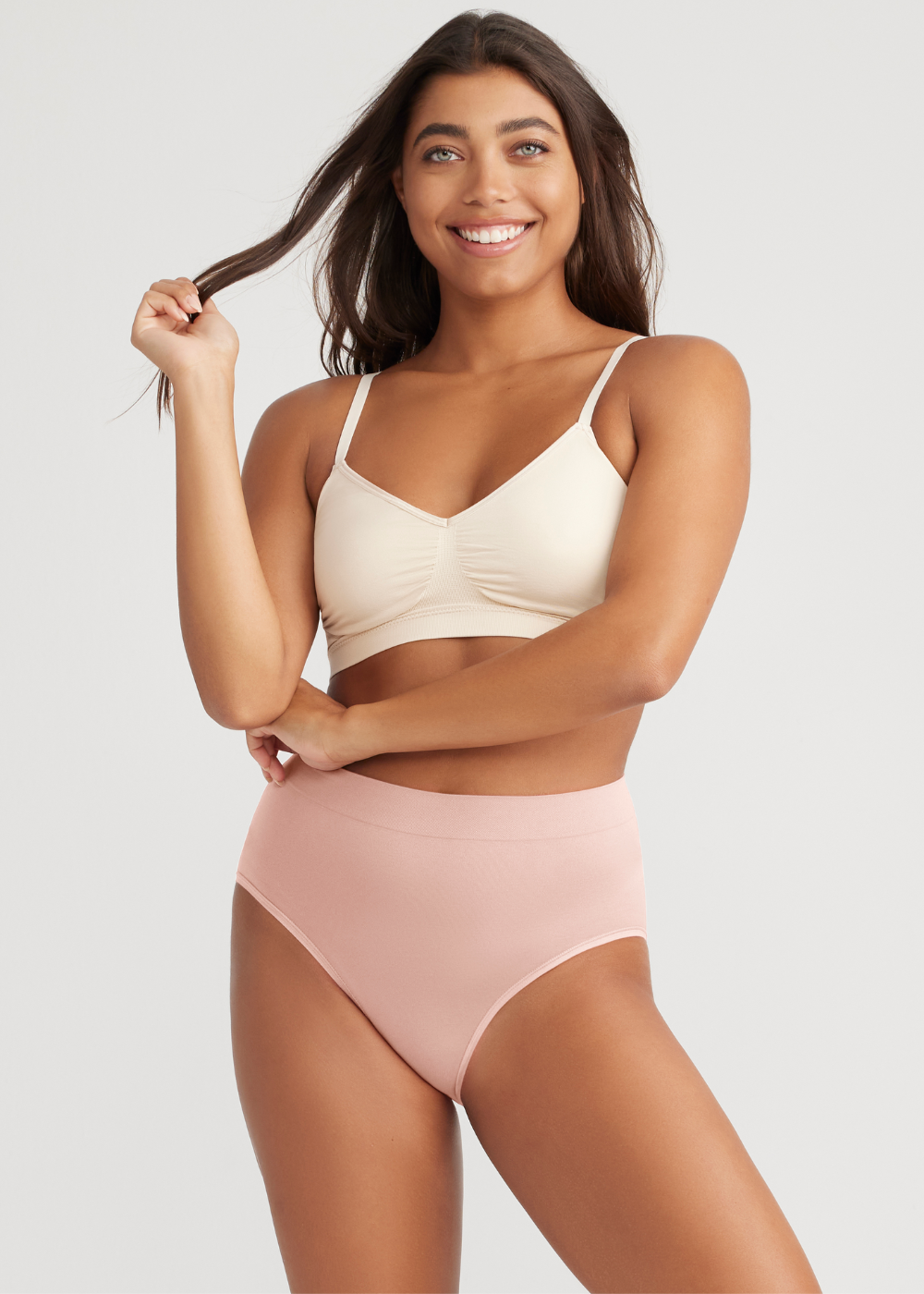 non-shaping retro brief - seamless in Pale Dogwood with emmie t-back bralette - outlast® seamless in Frappe worn by girl with left arm bent and touching right elbow, with right hand twirling hair. Yummie.