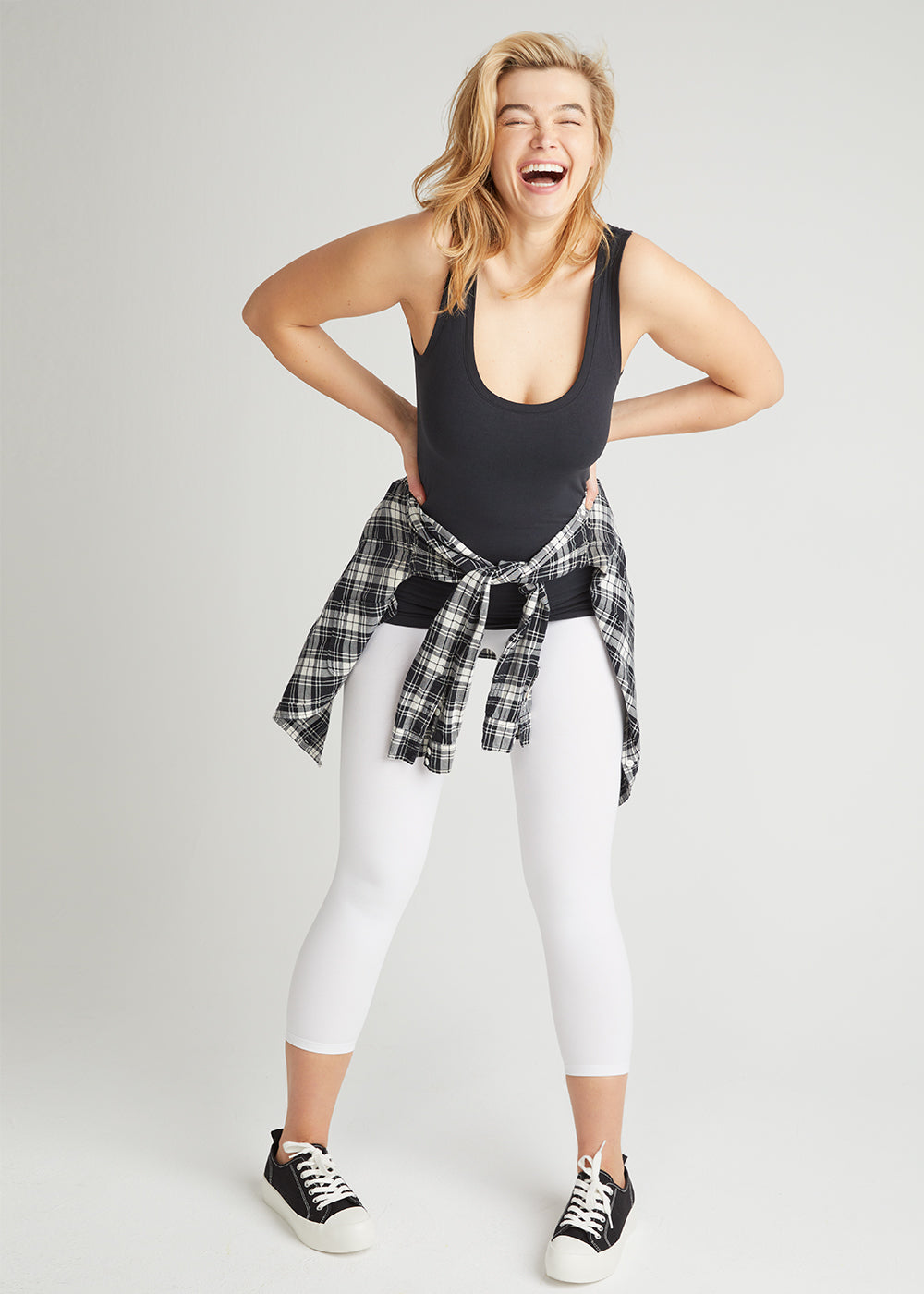 non-shaping tank - cotton seamless in Black,  gloria 7/8 ankle shaping legging - cotton stretch in White and a White & Black Plaid shirt worn by a woman standing facing forward hands at waist and bending slightly forward Yummie